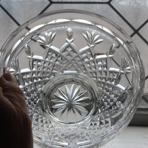 Puede incluir: Cuenco de cristal tallado transparente con intrincados patrones geom&eacute;tricos y florales. El cuenco se sostiene en una mano, mostrando las facetas y el dise&ntilde;o detallados. El dise&ntilde;o del cuenco incluye formas de diamante y patrones de estrella.