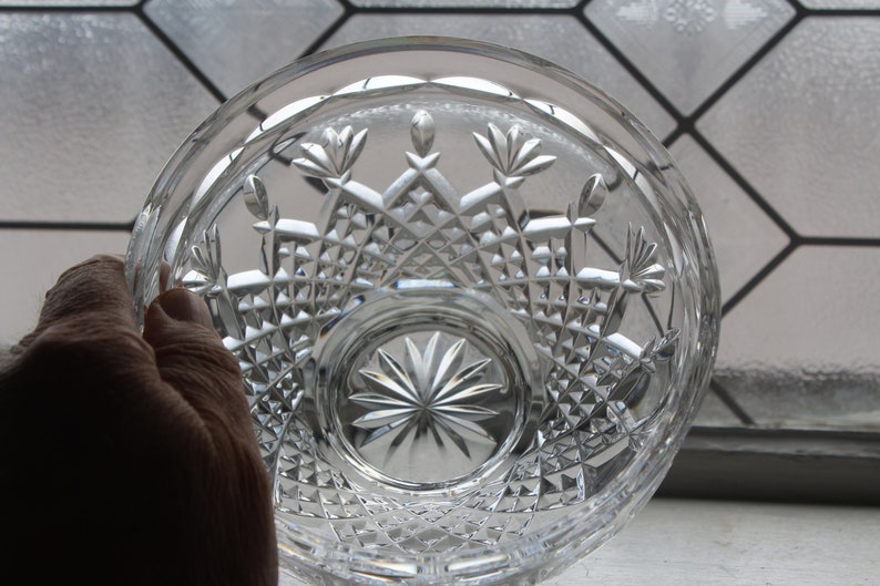 Puede incluir: Cuenco de cristal tallado transparente con intrincados patrones geom&eacute;tricos y florales. El cuenco se sostiene en una mano, mostrando las facetas y el dise&ntilde;o detallados. El dise&ntilde;o del cuenco incluye formas de diamante y patrones de estrella.