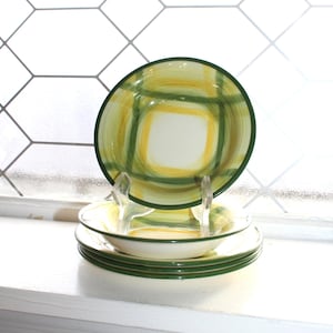 Op de afbeelding: Een set keramische borden en kommen met een groen, geel en wit ruitpatroon. De borden hebben een groene rand. De set bevat een groot bord, een kom en verschillende kleinere borden. De gerechten worden gepresenteerd op een wit oppervlak.