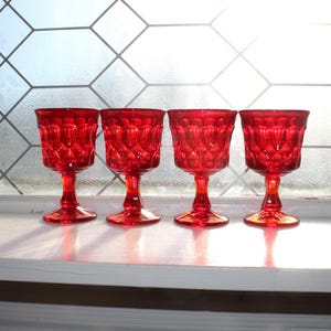 Puede incluir: Cuatro copas de vino vintage de color rojo rubí con un patrón de diamantes, sobre una superficie blanca. La cristalería está iluminada por la luz solar de una ventana con un diseño geométrico. Un clásico para cualquier bar.