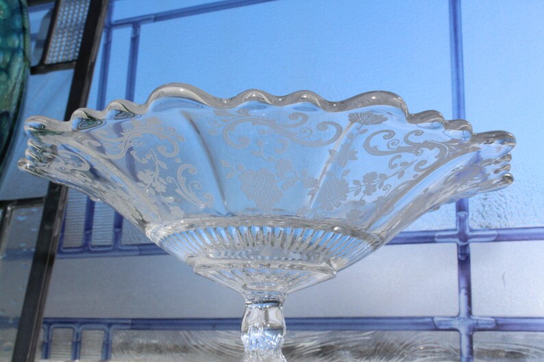 May include: A clear glass bowl with a scalloped edge and an etched floral design. The bowl is on a pedestal stand.