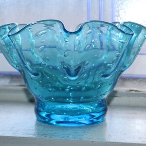 May include: A blue glass bowl with a ruffled rim and a textured surface. The bowl is filled with small bubbles.