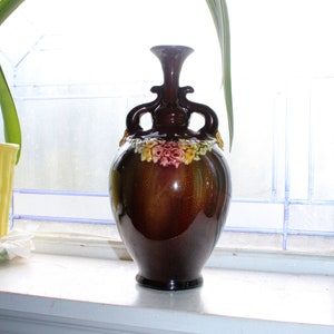May include: A brown ceramic vase with floral details and two handles. The vase has a glossy finish and is decorated with yellow, red, and green flowers.