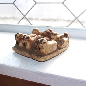 Puede incluir: Una pequeña escultura de cerámica blanca de un grupo de ovejas acurrucadas. La escultura está detallada con rasgos realistas y tiene un aspecto ligeramente desgastado.