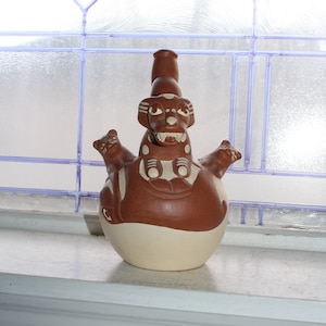 Puede incluir: Una figurita de cerámica marrón de un perro con dos perros más pequeños a cada lado. La figurita está decorada con detalles blancos y tiene una superficie texturizada.