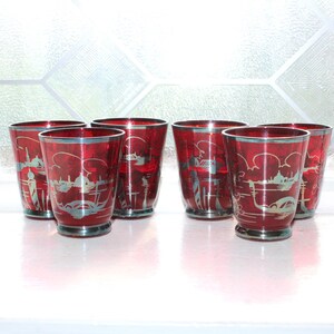 May include: A set of five ruby red glass tumblers featuring a silver etched design of a Venetian canal scene with gondolas and buildings. Each glass has a silver rim and a silver base, showcasing a consistent decorative motif across all pieces.