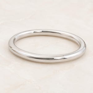 Può includere: Un anello in metallo color argento lucido con una fascia liscia e arrotondata. Il gioiello circolare presenta una finitura riflettente ad alta lucentezza che cattura la luce, mostrando un design semplice e continuo senza pietre o incisioni.