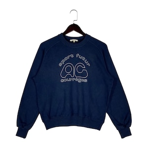 May include: Dark blue sweatshirt featuring white embroidered text and a logo. The text reads "sport futur" above the letters "AC" and the word "courr&egrave;ges" below. The sweatshirt is suspended from a wooden hanger.