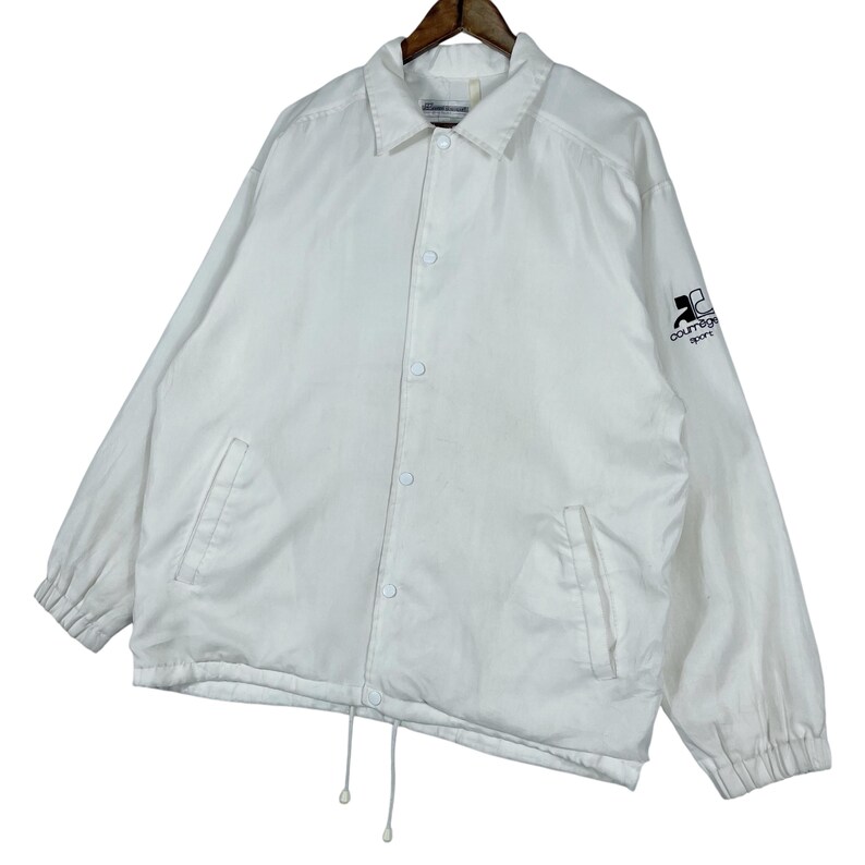 May include: White coach jacket with a button-up front, two front pockets, and a drawstring hem. The jacket features a collar and long sleeves with elastic cuffs. The Courr&egrave;ges Sport logo is on the upper left sleeve.