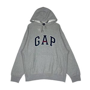 Puede incluir: Una taza de cerámica blanca con un asa negra y el texto "But First, Coffee" en un estilo manuscrito. La taza está sobre una superficie blanca. La taza mide aproximadamente 10 cm de alto.