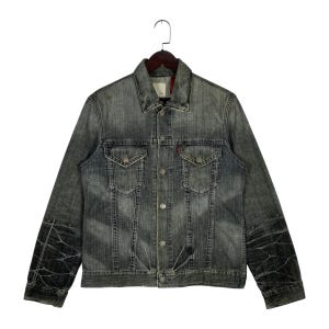May include: A faded black denim jacket with a button-up front, two chest pockets, and two side pockets. The jacket has a classic collar and long sleeves. The sleeves have a unique distressed pattern. The Levi's red tag is visible on the chest pocket.
