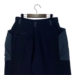 May include: Dark navy blue pants with two large pockets on the back, and two smaller pockets. The pants are hanging on a black hanger against a white background. The pockets are a darker shade of blue.