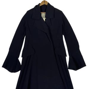 May include: A black coat with a unique design. The coat features a wide collar, long sleeves with flared cuffs, and a tailored waist. The coat is hanging on a wooden hanger. The overall style is elegant and sophisticated.