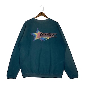 May include: Teal-colored sweatshirt with a rainbow star graphic and the text "LOST ENTERPRISES" on the back. The sweatshirt has a crew neck and long sleeves. The graphic features a star shape with a gradient of colors.