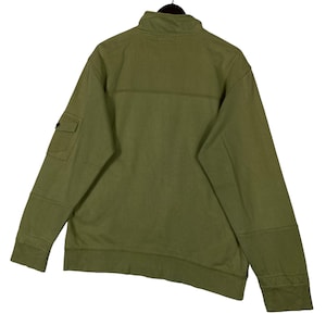 Puede incluir: Sudadera verde oliva con cremallera y cuello alto. Cuenta con un peque&ntilde;o bolsillo en la manga izquierda y coderas reforzadas. La vista trasera muestra la construcci&oacute;n y los detalles de costura de la prenda. Una prenda de abrigo informal y cotidiana.