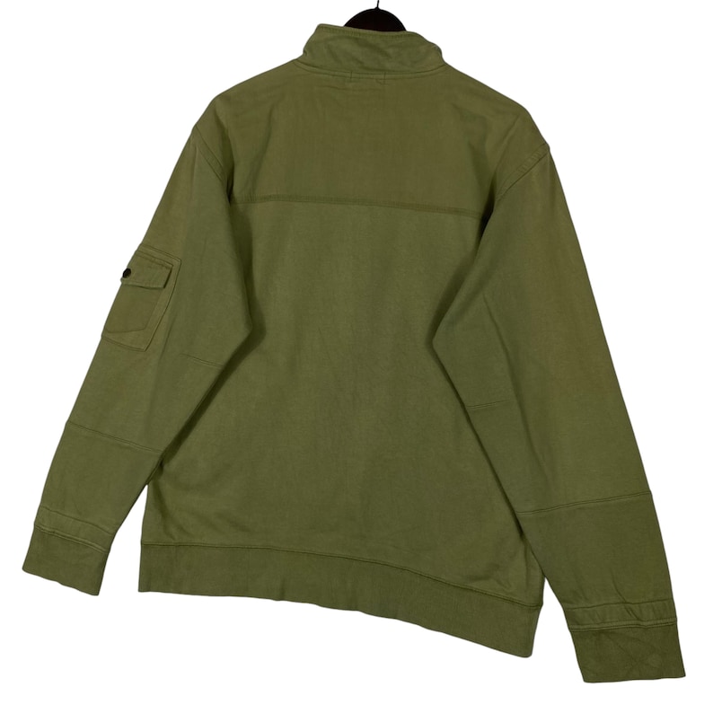 Puede incluir: Sudadera verde oliva con cremallera y cuello alto. Cuenta con un peque&ntilde;o bolsillo en la manga izquierda y coderas reforzadas. La vista trasera muestra la construcci&oacute;n y los detalles de costura de la prenda. Una prenda de abrigo informal y cotidiana.