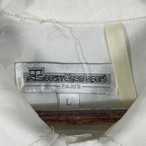 May include: White collared shirt with a tag that reads "courr&egrave;ges sport PARIS" in black text. The tag also has a logo and the size "L" printed on it. The shirt is made of a textured fabric.