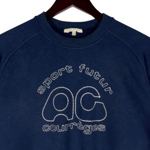 May include: Navy blue sweatshirt featuring the words "sport futur" and "courr&egrave;ges" in white, and the letters "ac" in a dotted design. The sweatshirt has a crew neck and raglan sleeves.