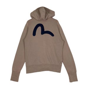 Puede incluir: Sudadera con capucha de color beige con un logotipo azul marino en la espalda. La sudadera tiene capucha, mangas largas y pu&ntilde;os acanalados. El logotipo es una forma curva estilizada.