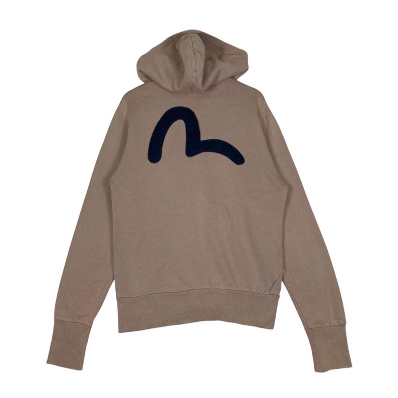 Puede incluir: Sudadera con capucha de color beige con un logotipo azul marino en la espalda. La sudadera tiene capucha, mangas largas y pu&ntilde;os acanalados. El logotipo es una forma curva estilizada.