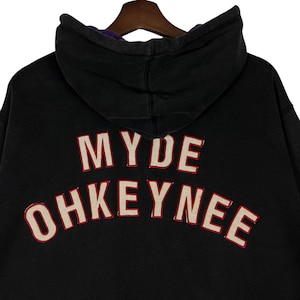 May include: Black hoodie with the text "MYDE OHKEYNEE" in white letters with a red outline. The hood has a purple lining. The hoodie is made of a soft material.