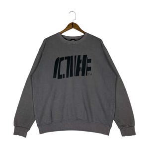 Könnte beinhalten: Ein graues Sweatshirt mit dem Wort "ACTIVE" in Schwarz auf der Brust. Das Wort ist in einer einzigartigen Schriftart gestaltet. Das Sweatshirt hat lange Ärmel und einen Rundhalsausschnitt. Es hängt an einem Holzkleiderbügel.