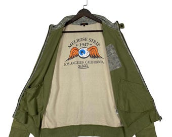Chaqueta bomber vintage Von Dutch verde oliva / Sudadera con cremallera y estampado Melrose Strip 1947 Flying Eyeball Graphic / Talla grande