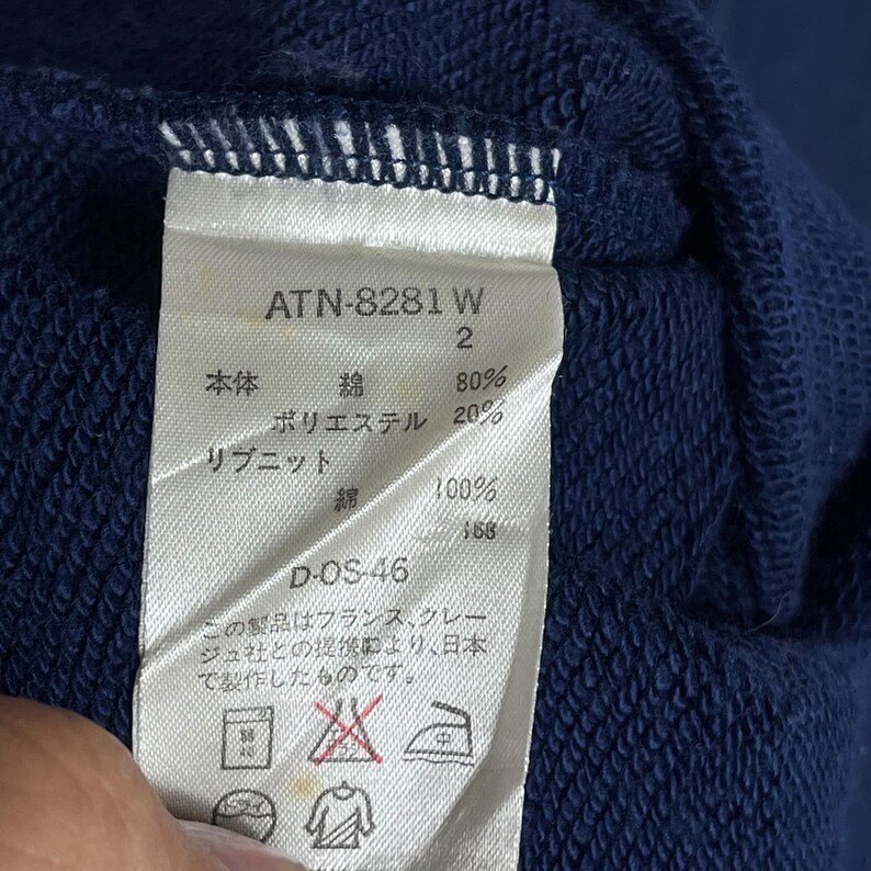 May include: A navy blue garment tag with Japanese text. The tag displays the product code ATN-8281 W, fabric composition percentages, and care symbols. The fabric is 80% cotton and 20% polyester.