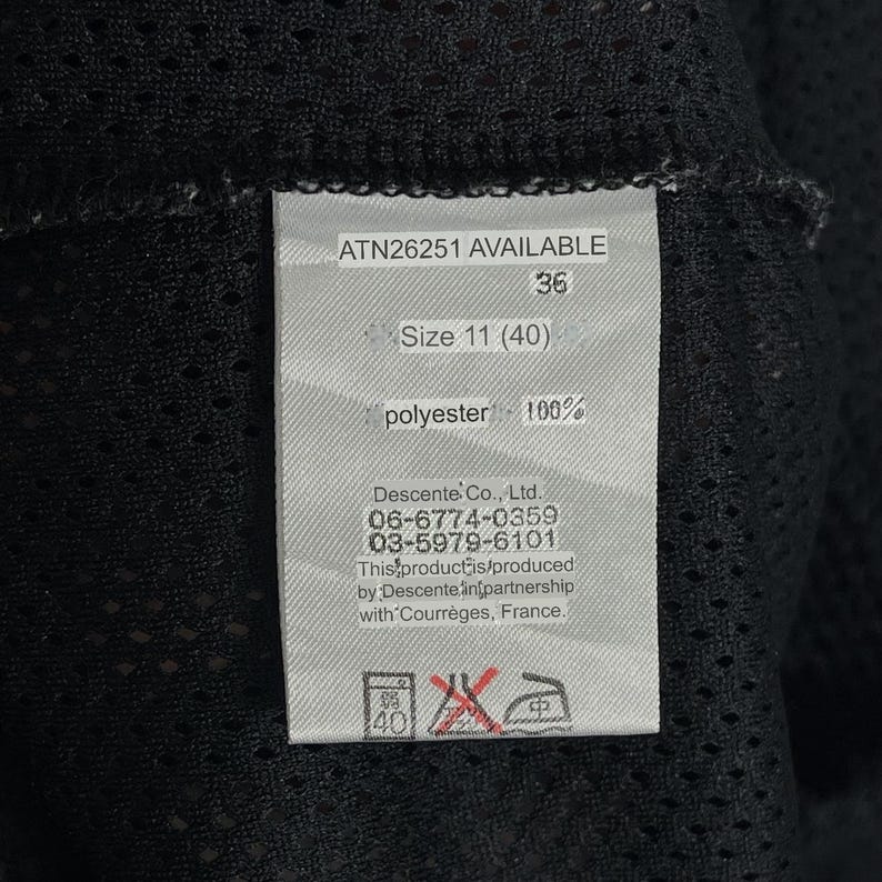 Pu&ograve; includere: Primo piano di un'etichetta con il testo "ATN26251 AVAILABLE", "36" e "Size 11 (40)". L'etichetta indica anche "polyester 100%" e include le informazioni del produttore. L'etichetta &egrave; attaccata a un tessuto a rete nero.