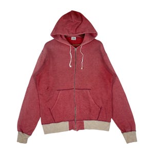 May include: A red zip-up hoodie with a hood and a front pocket. The hoodie features a drawstring and light grey bottom hem and cuffs. The fabric appears to be a soft, worn material.