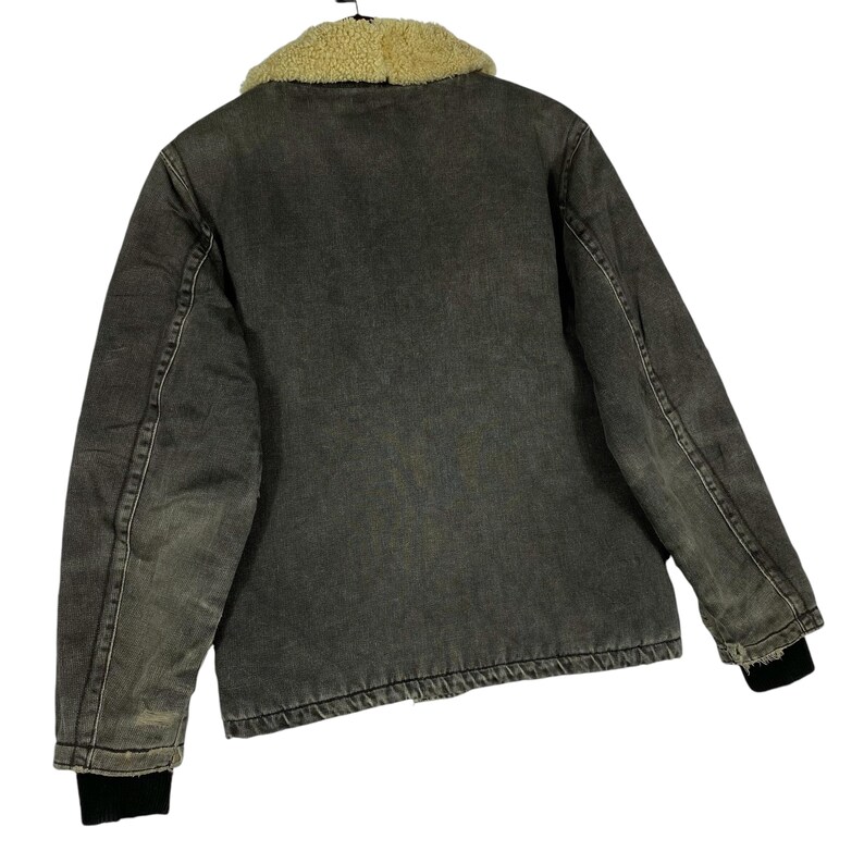 May include: A grey denim jacket with a tan sherpa collar. The jacket features black ribbed cuffs and a faded, worn look. The back view of the jacket is shown against a white background.