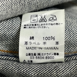 Puede incluir: Primer plano de una etiqueta de ropa blanca con texto japon&eacute;s y s&iacute;mbolos de cuidado, cosida en tejido vaquero. La etiqueta dice "100% algod&oacute;n" y "Made in Taiwan". La etiqueta tambi&eacute;n incluye instrucciones de lavado y un n&uacute;mero de tel&eacute;fono.
