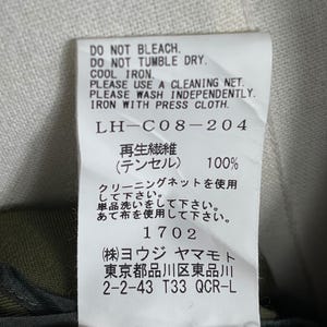 Puede incluir: Una etiqueta de tela blanca con texto negro que detalla las instrucciones de cuidado: No usar lej&iacute;a, No usar secadora, Planchar a baja temperatura. Incluye texto japon&eacute;s y el n&uacute;mero 1702. La etiqueta tambi&eacute;n enumera la direcci&oacute;n del fabricante.