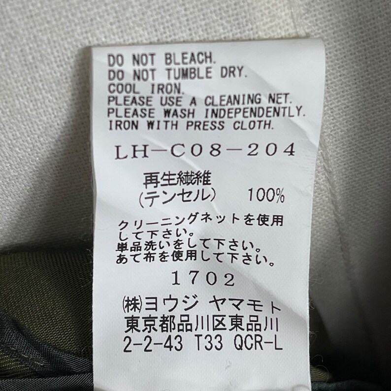 Puede incluir: Una etiqueta de tela blanca con texto negro que detalla las instrucciones de cuidado: No usar lej&iacute;a, No usar secadora, Planchar a baja temperatura. Incluye texto japon&eacute;s y el n&uacute;mero 1702. La etiqueta tambi&eacute;n enumera la direcci&oacute;n del fabricante.