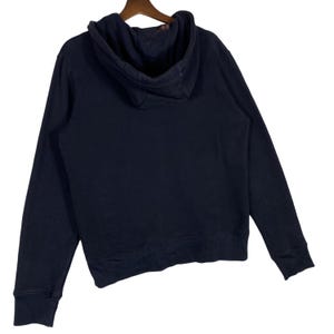 May include: A navy blue hoodie with a hood and long sleeves. The hoodie is hanging on a wooden hanger against a white background. The back of the hoodie is visible.