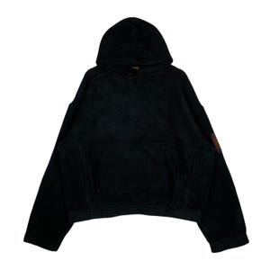 Könnte beinhalten: Schwarzer Kapuzenpullover mit Kängurutasche und Kapuze mit Kordelzug. Der Pullover hat lange Ärmel und einen verkürzten Saum. Ein kleiner Aufnäher mit orangefarbenen und braunen Farben befindet sich am linken Ärmel.