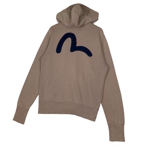 Puede incluir: Sudadera con capucha de color beige con un logotipo azul marino en la espalda. La sudadera tiene capucha, mangas largas y pu&ntilde;os acanalados. El logotipo es un dise&ntilde;o curvo estilizado.