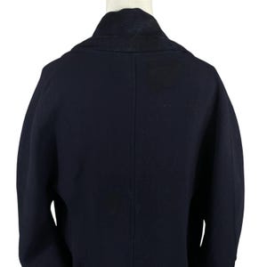 May include: A navy blue coat with a wide collar and a tailored fit. The back of the coat is visible, showcasing the clean lines and structured design. The coat is displayed on a mannequin, highlighting its shape and style.