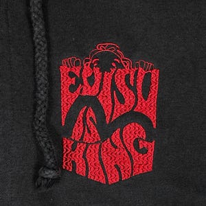 May include: Black hoodie with a red embroidered design. The design features the text "EVISU KING" in a stylized font within a rectangular shape. The hoodie has a black drawstring.