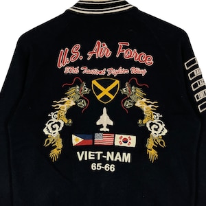 May include: Black bomber jacket with embroidered "U.S. Air Force" text, dragons, flags, and "VIET-NAM 65-66" text. The jacket has a white and black striped collar and cuffs. The back of the jacket features a variety of patches.