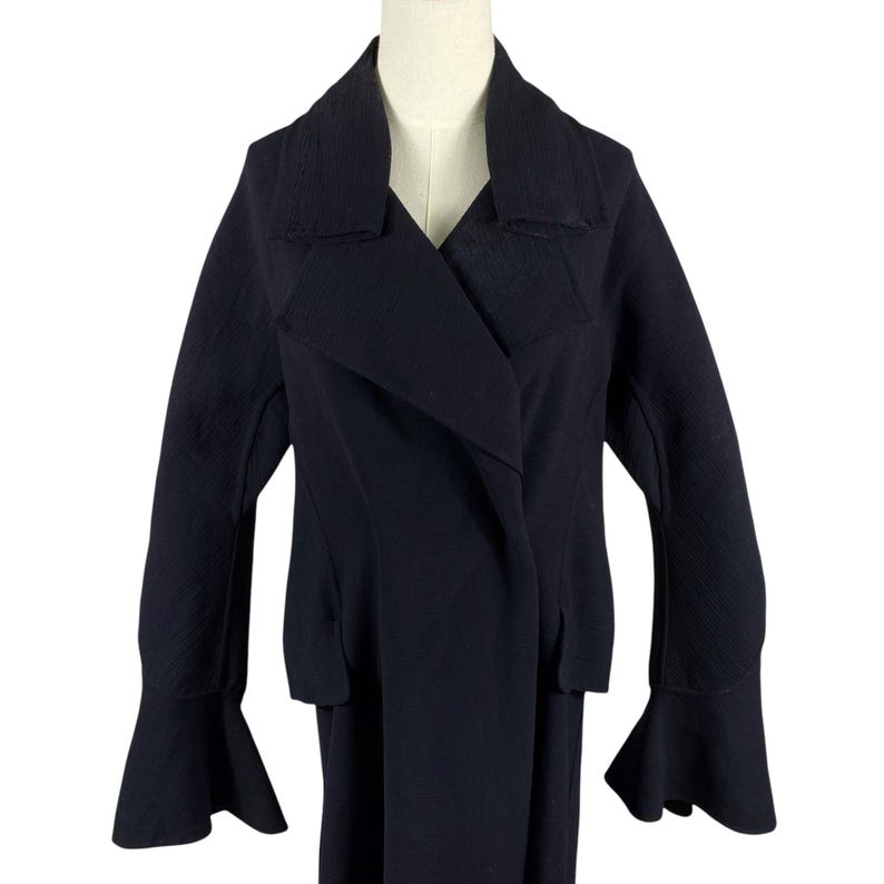 May include: A dark navy blue jacket with a unique design. The jacket features a wide lapel, a double-breasted closure, and flared sleeves. The garment is displayed on a mannequin against a white background.