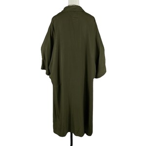 Puede incluir: Chaqueta larga verde oliva estilo kimono con mangas anchas y cuello. Vista trasera de la prenda sobre un maniqu&iacute; blanco. La tela parece ser un material ligero.