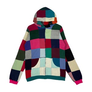 May include: A colorful patchwork zip-up hoodie with a hood and a kangaroo pocket. The hoodie features a vibrant mix of squares in various colors, including pink, blue, green, and red. The cuffs are bright pink.