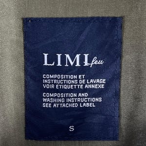 Puede incluir: Una etiqueta azul marino con el nombre de la marca "LIMI feu" en letras blancas. El texto en franc&eacute;s e ingl&eacute;s detalla la composici&oacute;n y las instrucciones de lavado. La etiqueta, marcada con una "S", est&aacute; sobre una tela verde oliva.