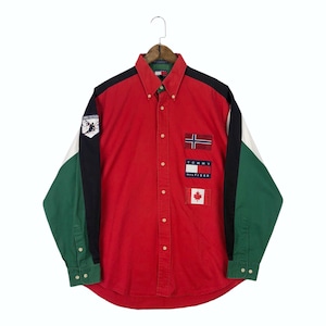 May include: A long-sleeve button-down shirt featuring a red main body with black and green colour-blocked sleeves. The shirt displays patches including the Norwegian flag, the Canadian flag, and a Tommy Hilfiger logo on the front and sleeve.