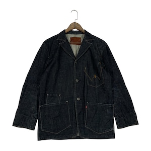 Puede incluir: Chaqueta vaquera azul oscuro con dise&ntilde;o de blazer. Cuenta con solapa con muescas, cierre de tres botones y m&uacute;ltiples bolsillos, incluidos dos grandes bolsillos de parche en la cintura. Una peque&ntilde;a etiqueta roja es visible en un bolsillo. La chaqueta est&aacute; colgada de una percha de madera.
