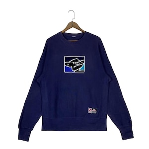 May include: Navy blue sweatshirt with a square graphic on the front. The graphic features a stylized design in black, white, blue, and teal. The sweatshirt has long sleeves and a crew neck.