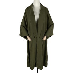 Puede incluir: Bata estilo kimono verde oliva con un ajuste relajado. La bata presenta un cuello chal, mangas largas y dos bolsillos delanteros. Un cierre de bot&oacute;n &uacute;nico se encuentra en la cintura. La bata se exhibe en un maniqu&iacute;.