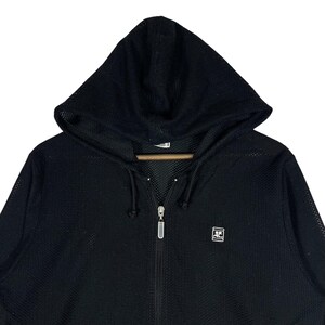 Pu&ograve; includere: Felpa con cappuccio nera con cerniera e texture a rete. La felpa con cappuccio ha un cordoncino, un cappuccio e un piccolo logo sul petto. La cerniera &egrave; color argento.