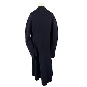 May include: A long, navy blue coat with a classic design. The coat is displayed on a mannequin, showcasing its full length and tailored silhouette. The coat features a simple, elegant style, suitable for various occasions.